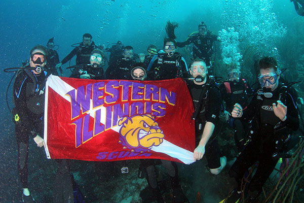 group of WIU SCUBA divers underwater holding Western Illinois flag