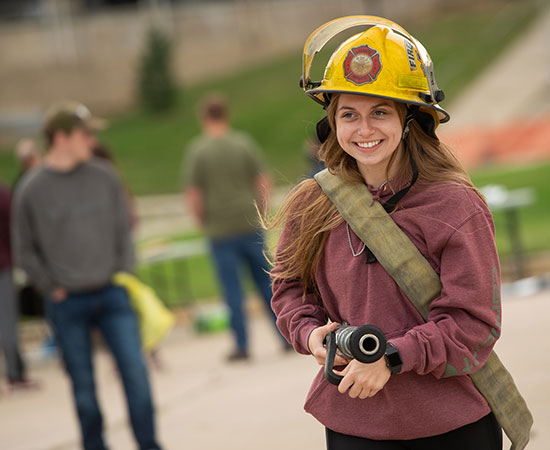 student holding fire hose and wearing protective hat