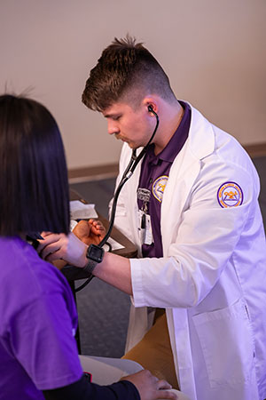 a student in a lab coat checking someone's blood pressure