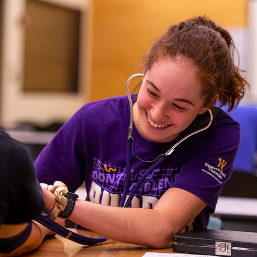 a student in a classroom checking someone's blood pressure