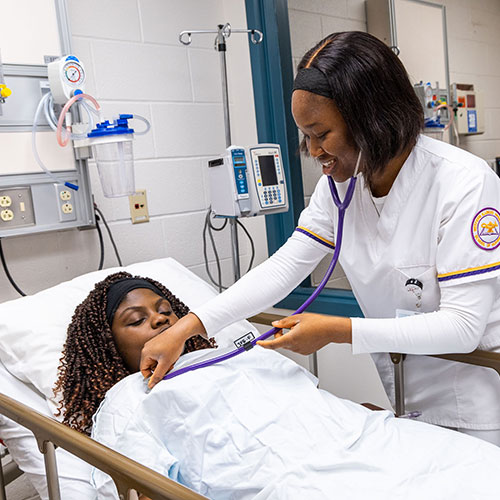 a student in a hospital setting, checking the heart rate of a patient