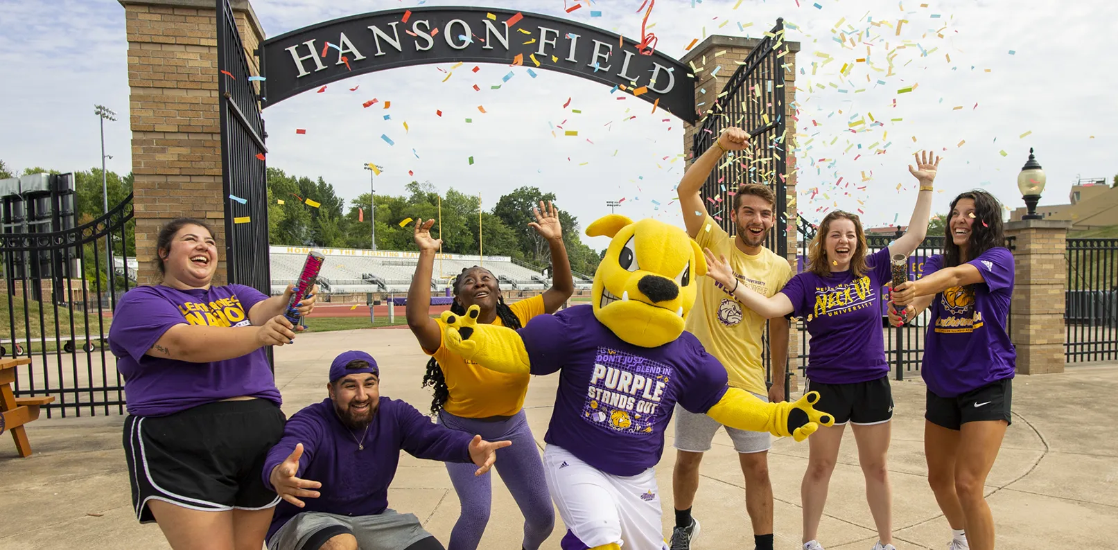 Group of students celebrating with Rocky (costumed mascot) in front of Hanson Field gateway entrance