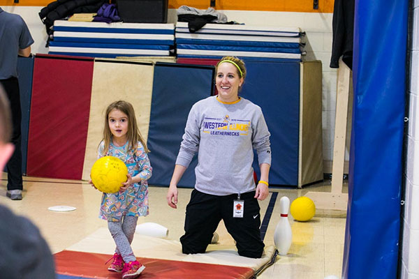 student demonstrating bowling in a gym with a young child
