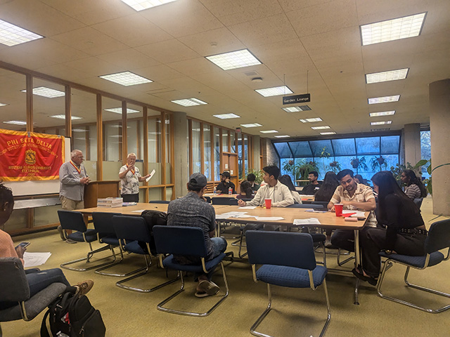 group of about 18 students sitting at tables listening to presentation in the university library