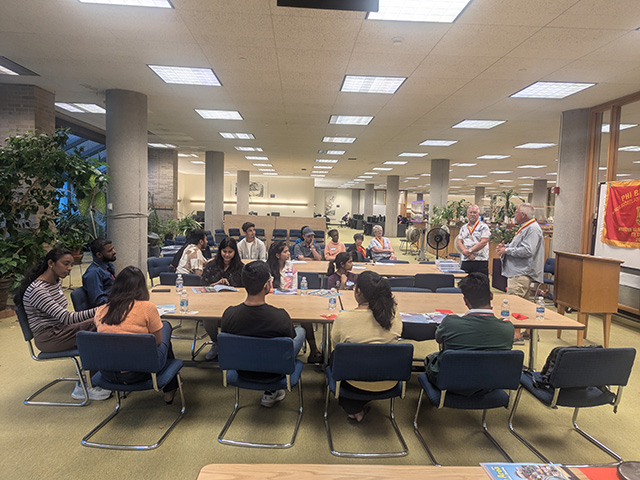 group of about 18 students sitting at tables listening to presentation in the university library